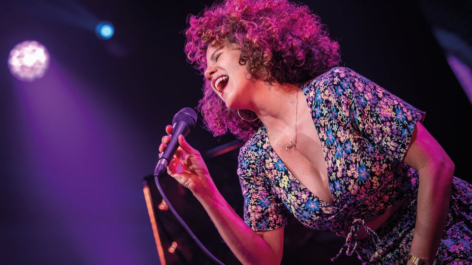 Foto vom Event von Cyrille Aimée mit der Künstlerin mit lockigem Haar, die mit einem Mikrofon singt