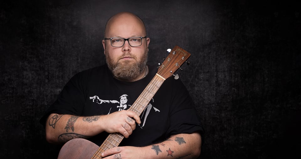 Mann mit einer Gitarre in der Hand vor schwarzem Hintergrund