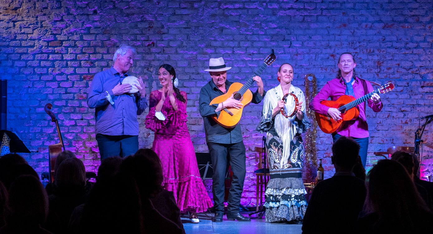 Foto von fünf Personen auf einer Flamenco-Bühne mit traditionellen Kostümen und einer Gitarre.