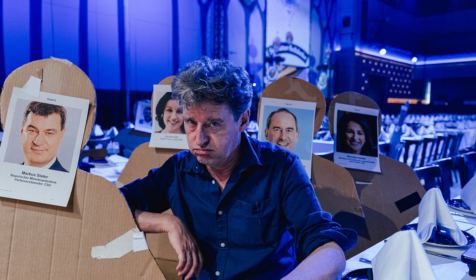 Mann sitzt zwischen Kartonagen die mit Gesichtern von Politikern verziert sind
