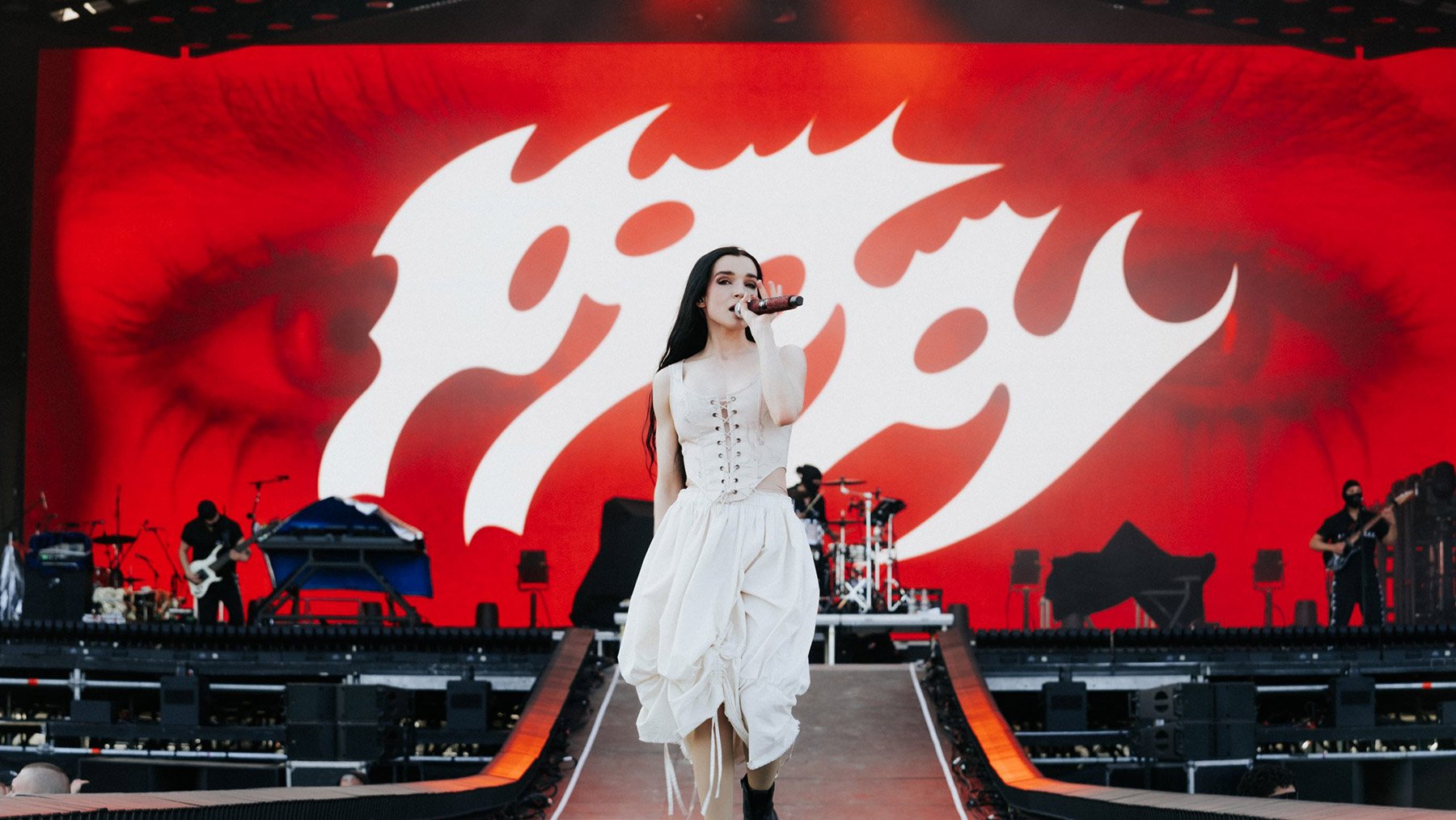 Poppy live auf der Bühne – mit rotem Bildschirm im Hintergrund und markanter Typografie.