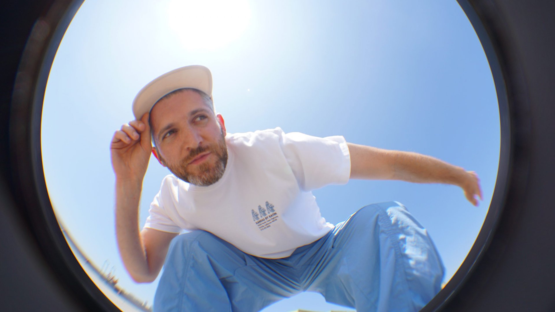 Ein Mann in weißem Shirt, blauer hose und weißer Kappe schaut durch ein rundes Fenster