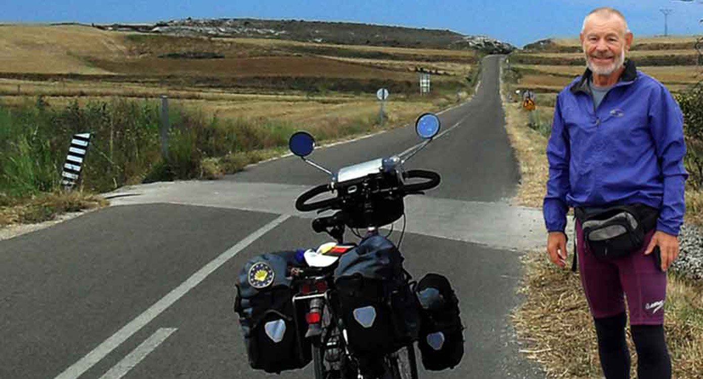 Foto von einem Mann auf einer Straße mit einem Fahrrad und angebauten Gepäcktaschen für das Event ‚Multivisionsshow über den Jakobsweg