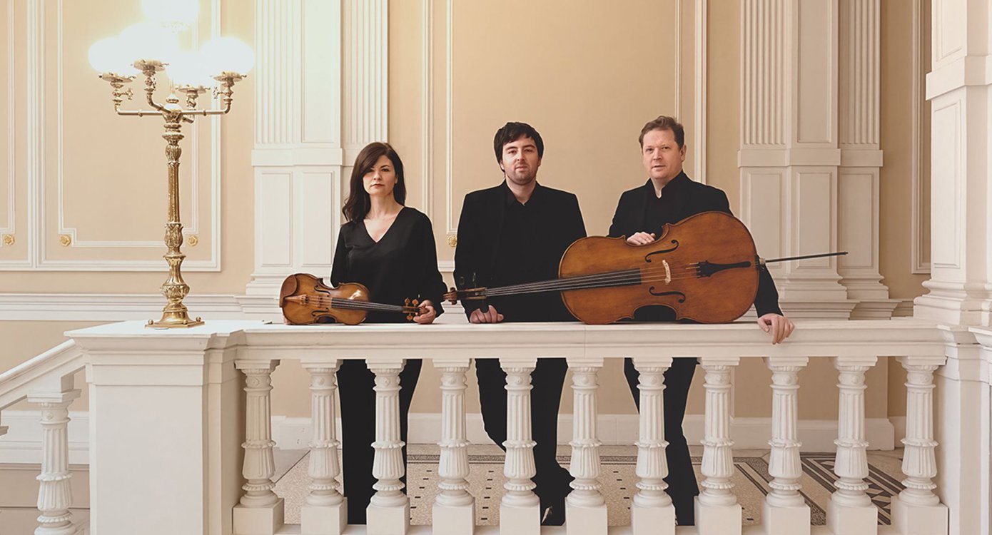 Foto der Gruppe „Guadagnini Trio“, in einem Gebäude im klassischen Stil. Sie sind in Schwarz gekleidet und haben Saiteninstrumente.
