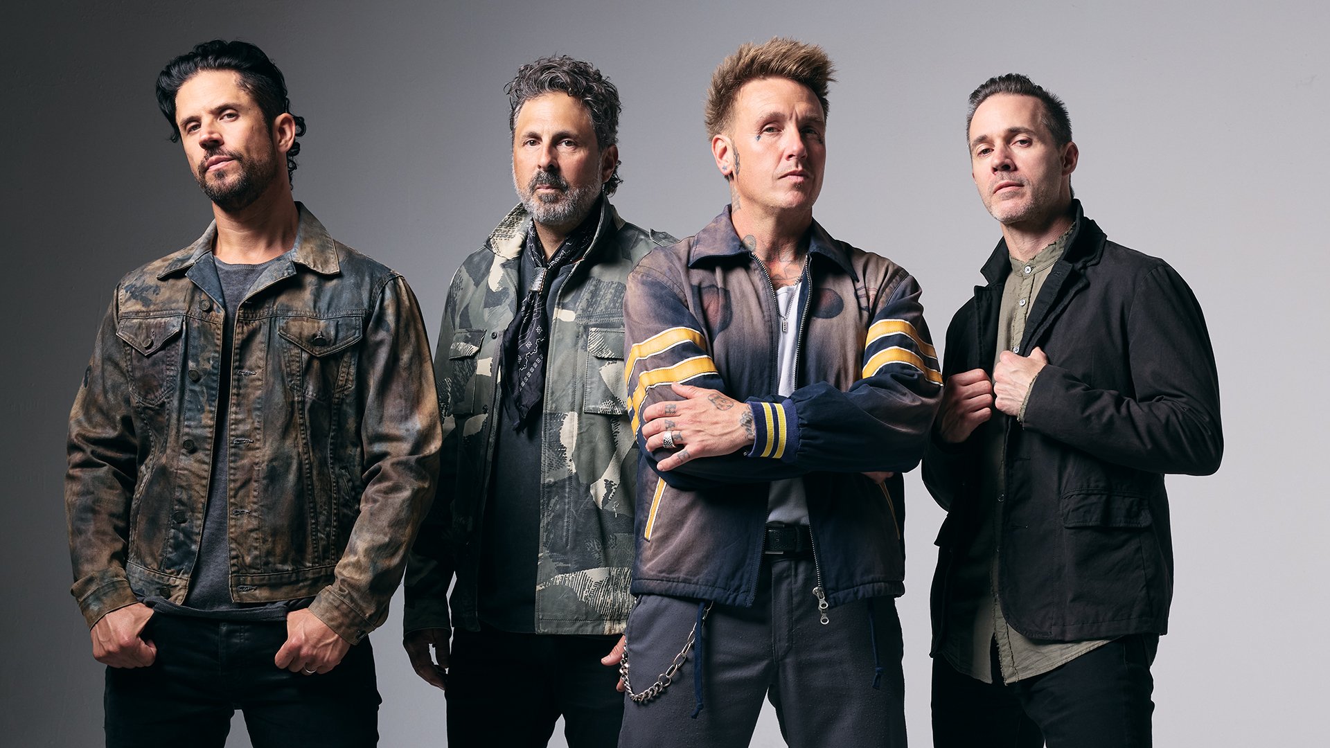 Bandfoto von Papa Roach: Vier Musiker stehen nebeneinander vor grauem Hintergrund, tragen dunkle Kleidung im Rockstil; einer im Vordergrund mit verschränkten Armen.