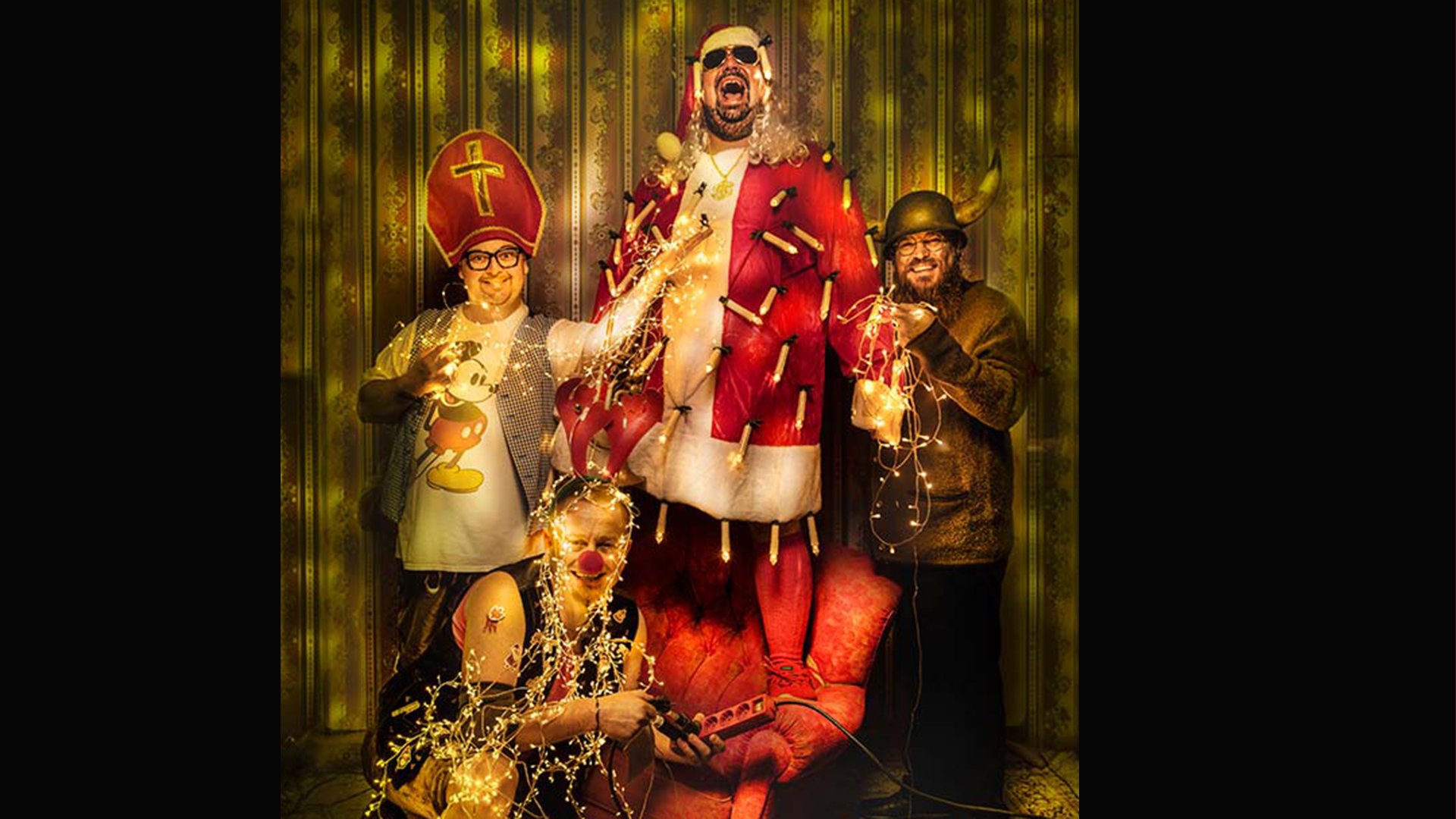 Vier Kabarettisten in weihnachtlichen Kostümen stehen und sitzen vor goldener Tapete mit Lichterketten; zentrale Figur als Nikolaus verkleidet – Werbemotiv zum Weihnachtsprogramm „O‘ghängt is!“ von Da Meier & Watschnbaam.