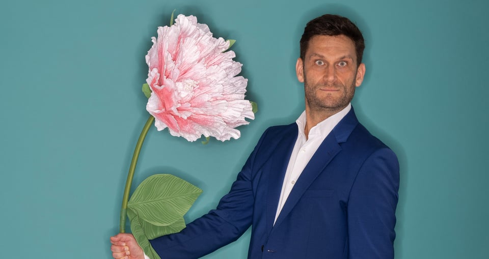 Christian Ehring mit einer großen Blume in der Hand vor blauem Hintergrund
