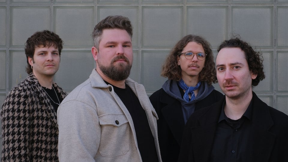 Die vier Bandmitglieder vor einer hellen Vertägelung