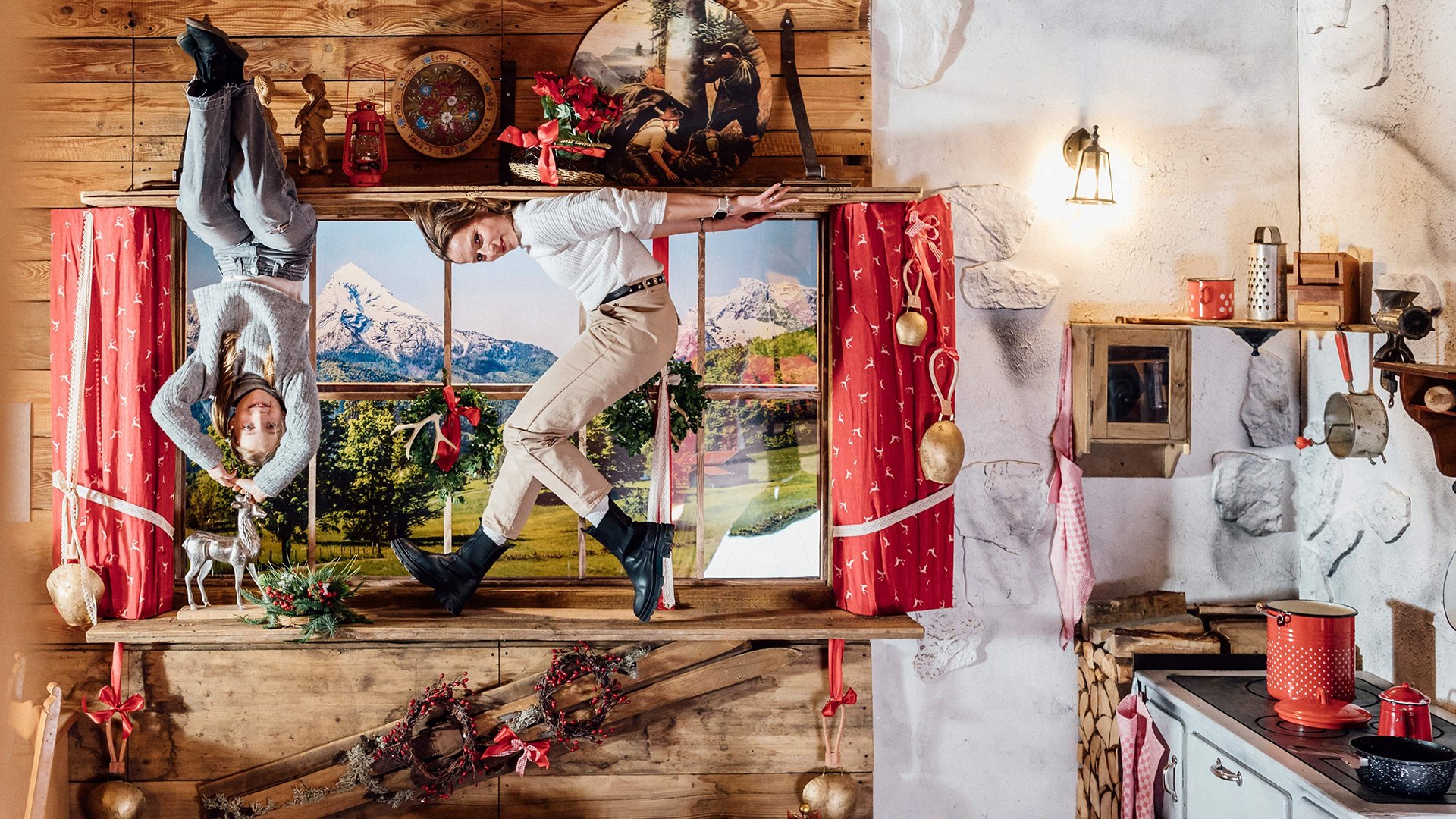 Zwei Personen "hängen" mit den Füßen an der Decke eines traditionell bayrisch eingericheten Raumes