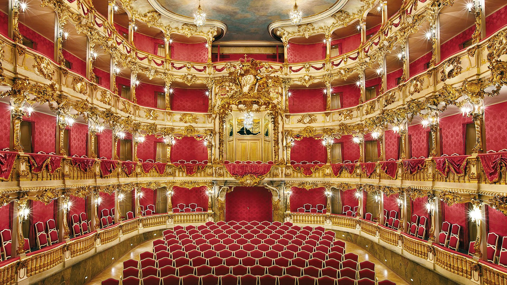 Prunkvoller Theatersaal mit roten Sitzen, roten Logen und reich verzierten goldenen Rokoko-Elementen auf mehreren Rängen. Zentraler Blick in den Zuschauerraum des Cuvilliés-Theaters.