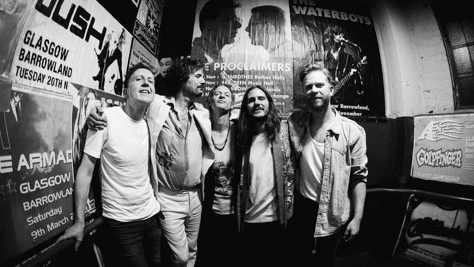 The Temperance Movement, fünfköpfige Rockband aus Glasgow, stehen eng beieinander in einem Backstagebereich mit Konzertplakaten an den Wänden, schwarz-weißes Gruppenfoto – Pressebild zur „Let It All Out“-Tour