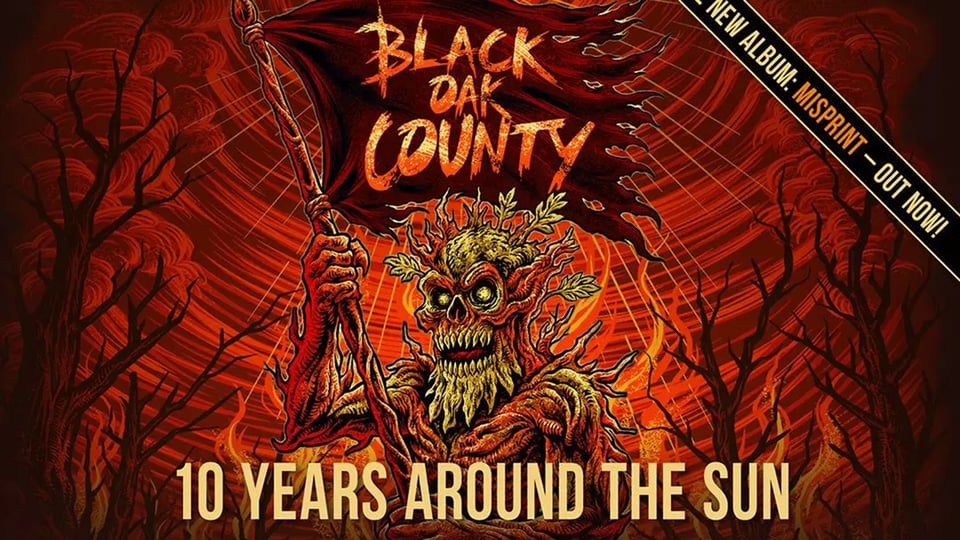 Plakatmotiv von Black Oak County mit den Aufschriften Black Oak County, 10 Years Around The Sun Im Zentrum steht eine düstere baumartige Kreatur mit Fahne vor einer rot orangefarbenen Waldkulisse mit Flammen und kahlen Bäumen.