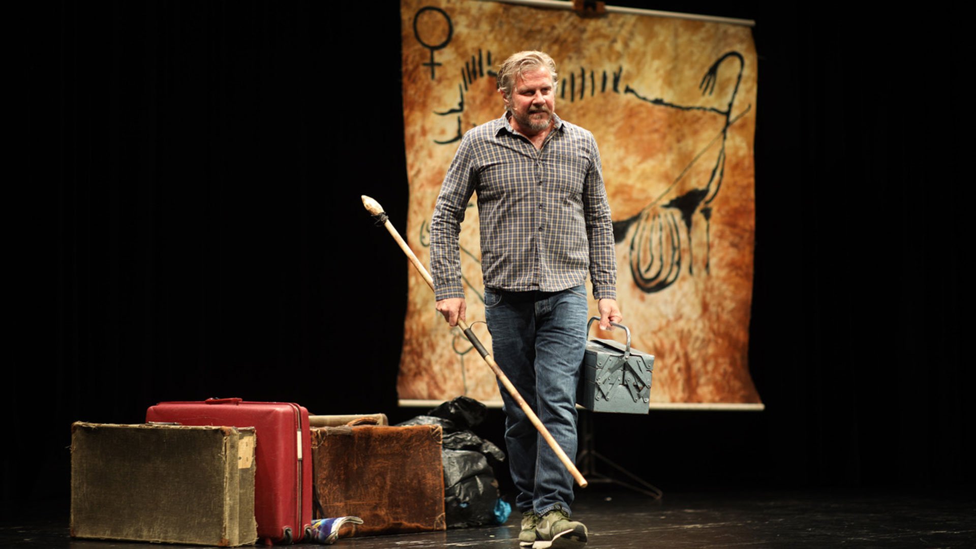 Foto für das Event mit dem Künstler auf der Bühne, im Hintergrund stehen vintage Koffer und eine prähistorische Felsmalerei