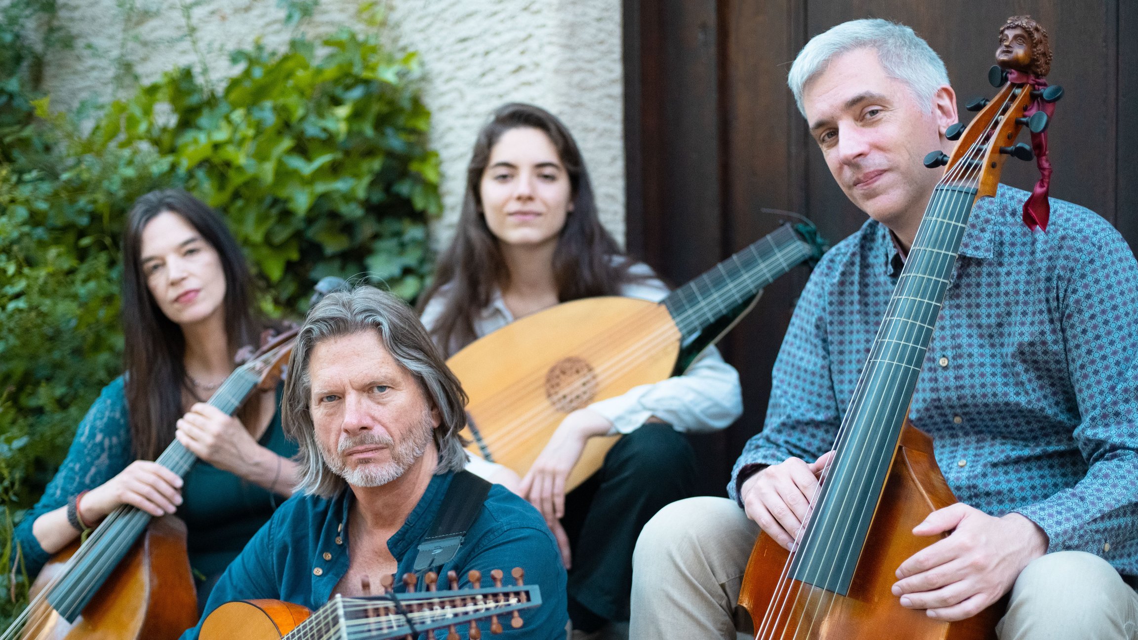 Das Ensemble Phoenix Munich mit vier Musikerinnen und Musikern auf einer Treppe im Freien, mit Viola da Gamba, Theorbe und Bassgambe vor einer Hauswand mit Begrünung.