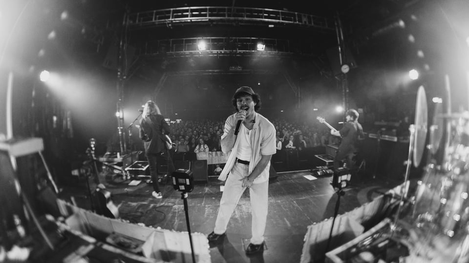 Schwarz‑Weiß‑Foto des Künstlers Marten auf einer Bühne mit Fisheye‑Effekt.