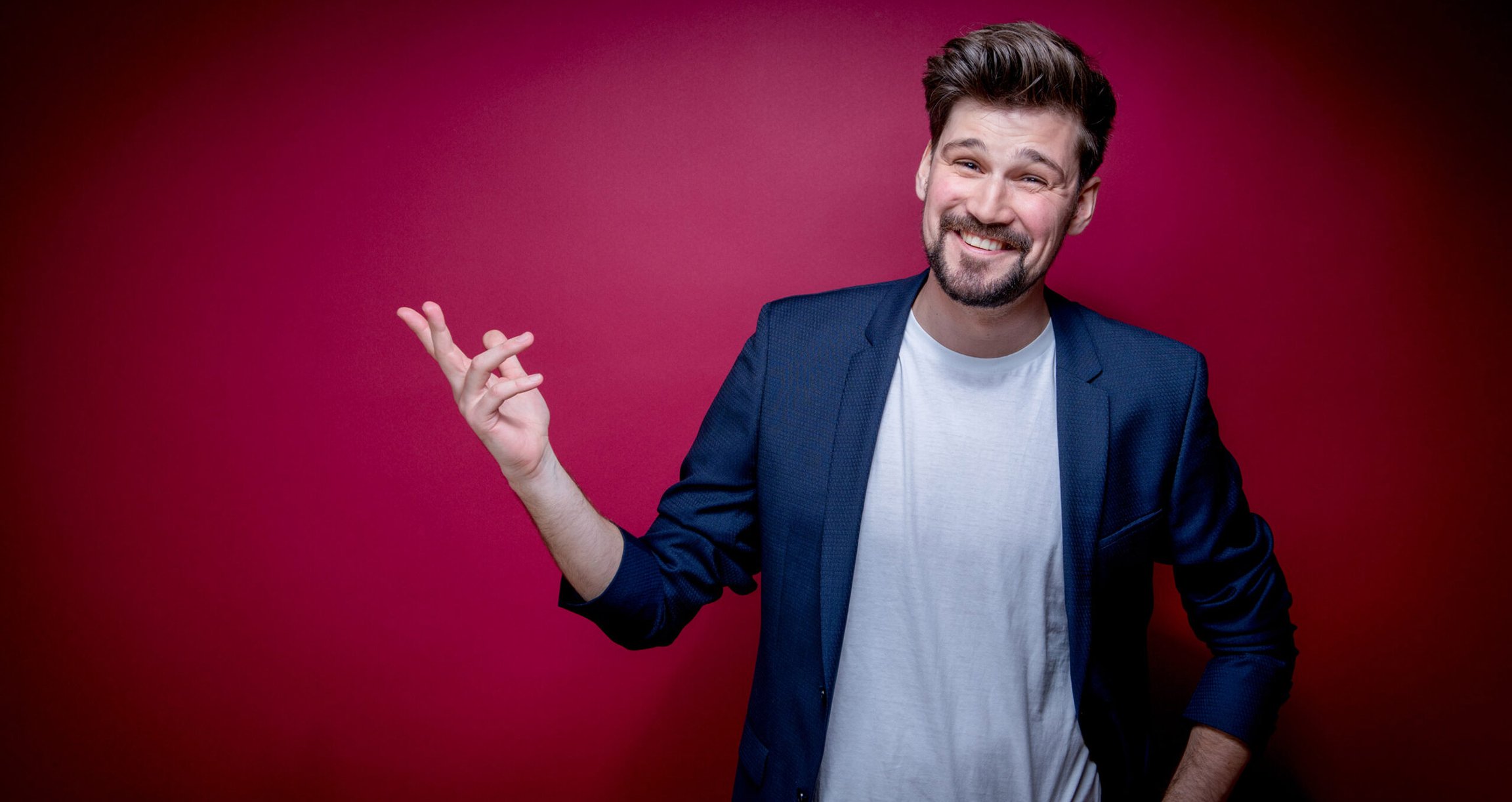 Mann in blauem Sakko und weißem Shirt lachend vor rotem Hintergrund