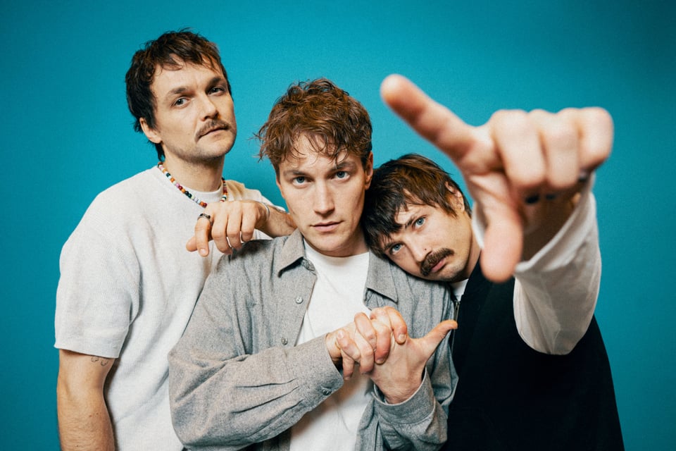 Drei junge Männer in Freizeitkleidung vor blauem Hintergrund