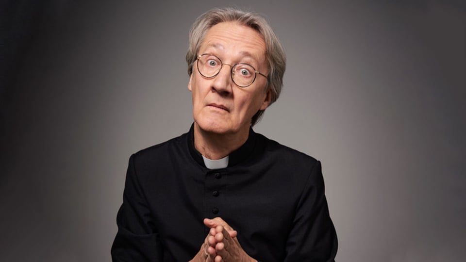 Foto für die Veranstaltung von Holger Paetz mit dem Künstler als Priester gekleidet vor grauem Hintergrund.