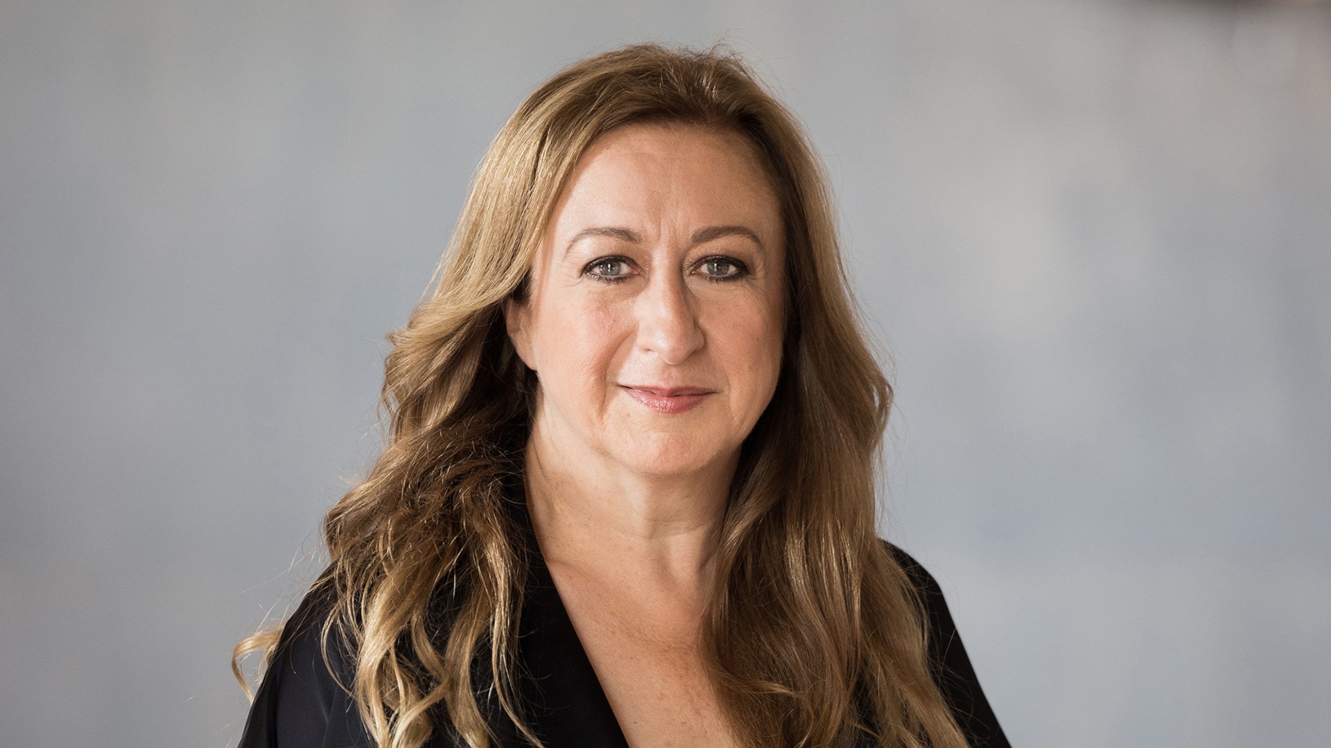 In Portrait von Simone Young in schwarzem Oberteil vor hellgrauem Hintergrund