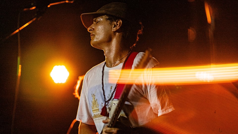 Der Künstler in weißem Shirt mit Kappe und Gitarre auf einer Bühne im Scheinwerferlicht