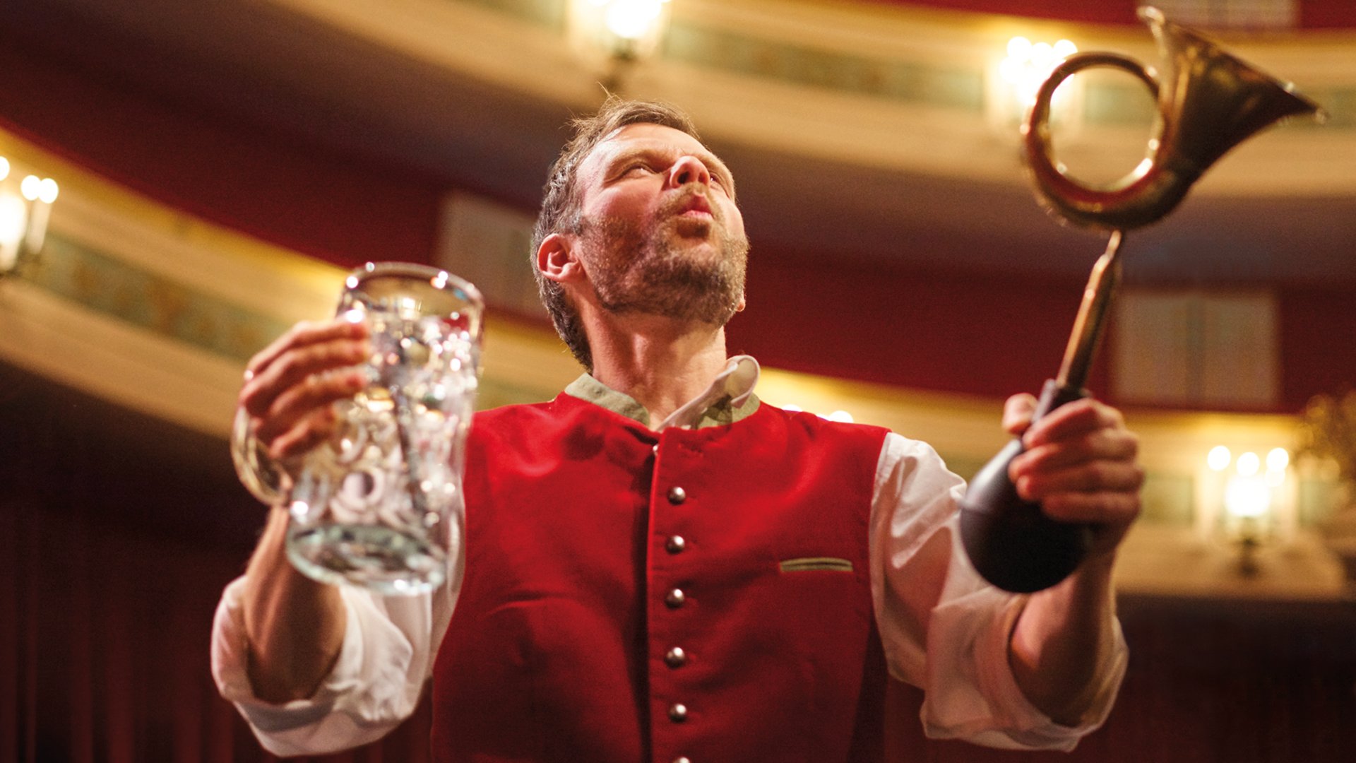 Foto für die Veranstaltung Opern auf Bayrisch, mit einem Mann, der ein Bier in der Hand hält