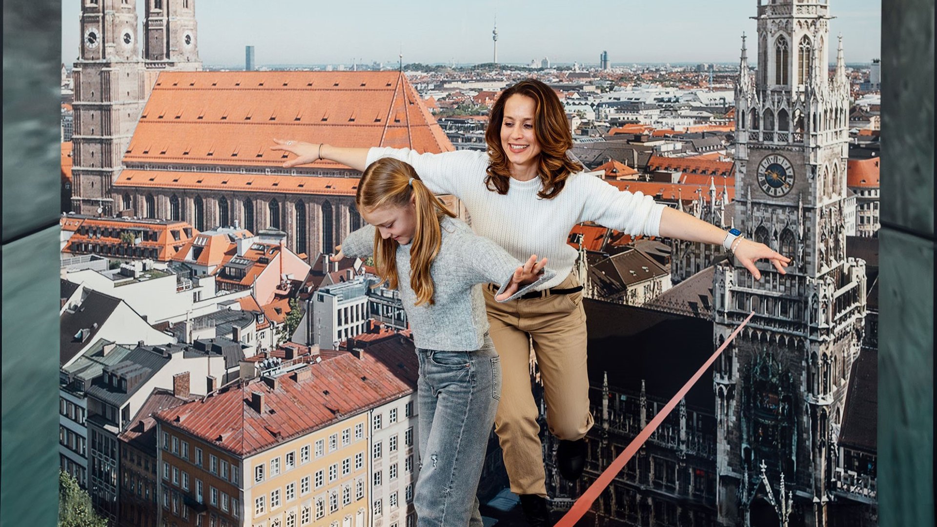 Eine Frau und ein Mädchen balancieren auf einer Slackline, im Hintergrund München