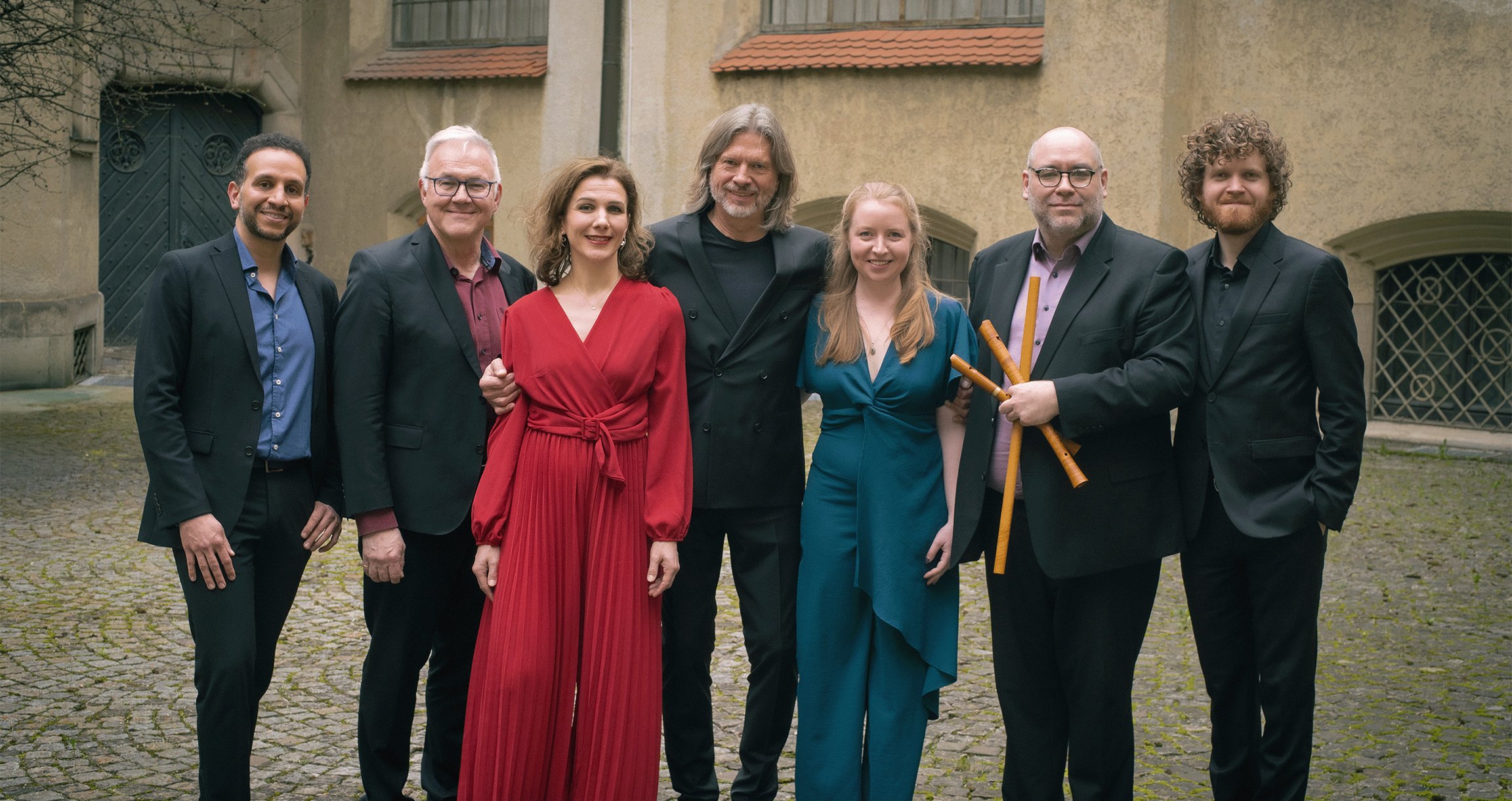 Sieben Personen in historischem Innenhof, fünf Herren in dunklen Anzügen, zwei Damen und farbiger Kleidung