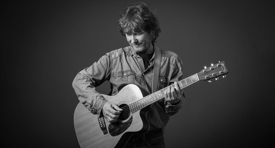 Schwarz-weiss Bild von Mann in Jeanshemd mit Akustikgitarre