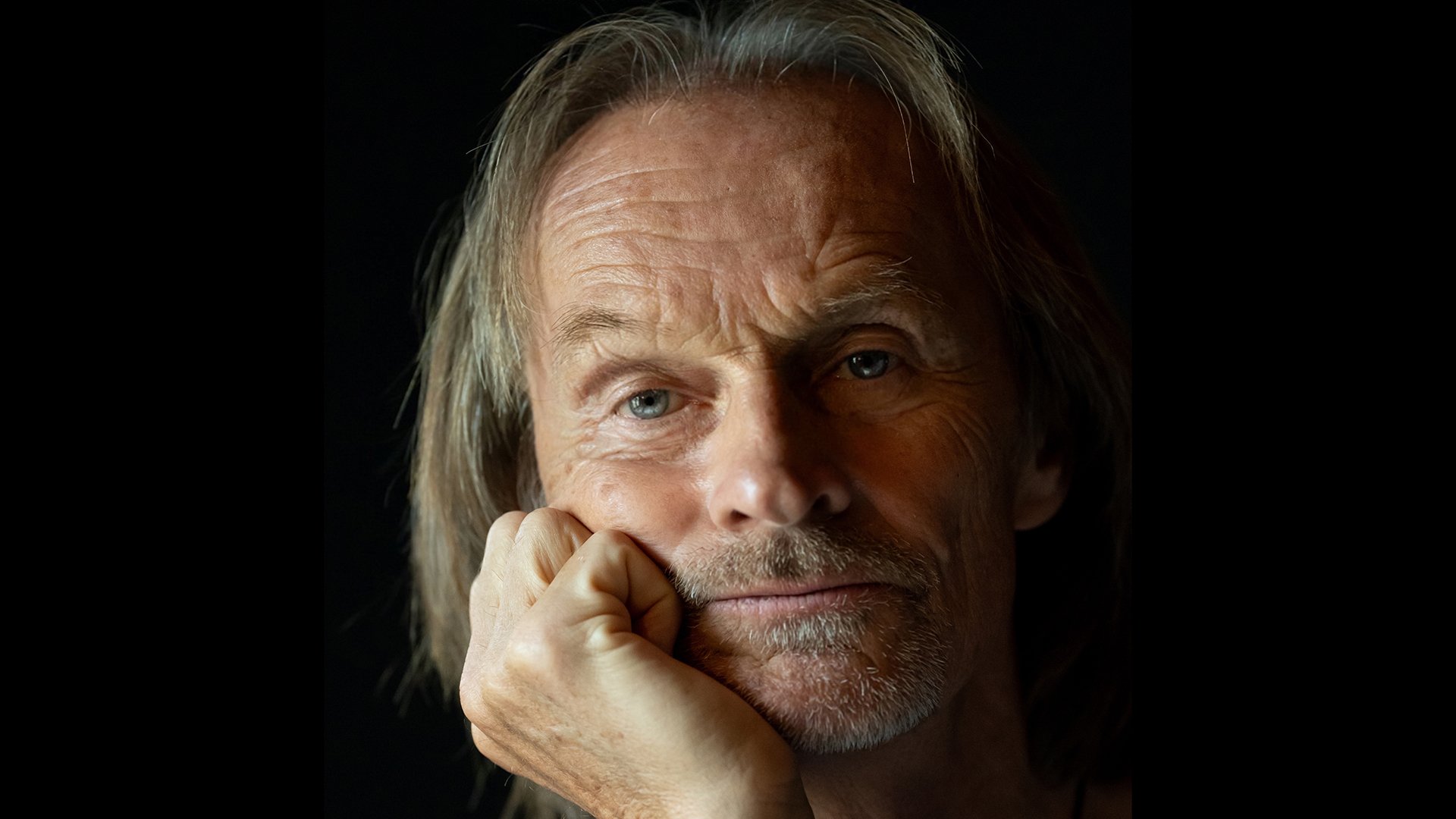 Portrait des Künstlers, der seine Hand auf das Kinn stützt, mit schwarzem Hintergrund