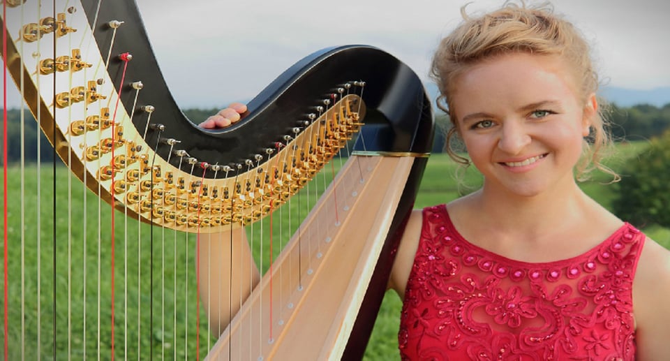 Dame in rotem Kleid mit Harfe auf Wiese, im Hintergrund Berge