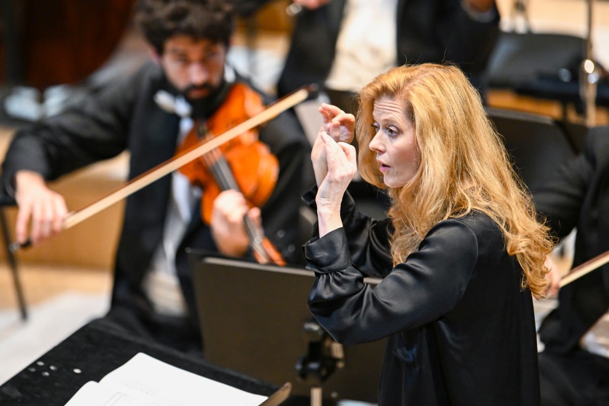 eine rothaarige Frau dirigiert ein Orchester