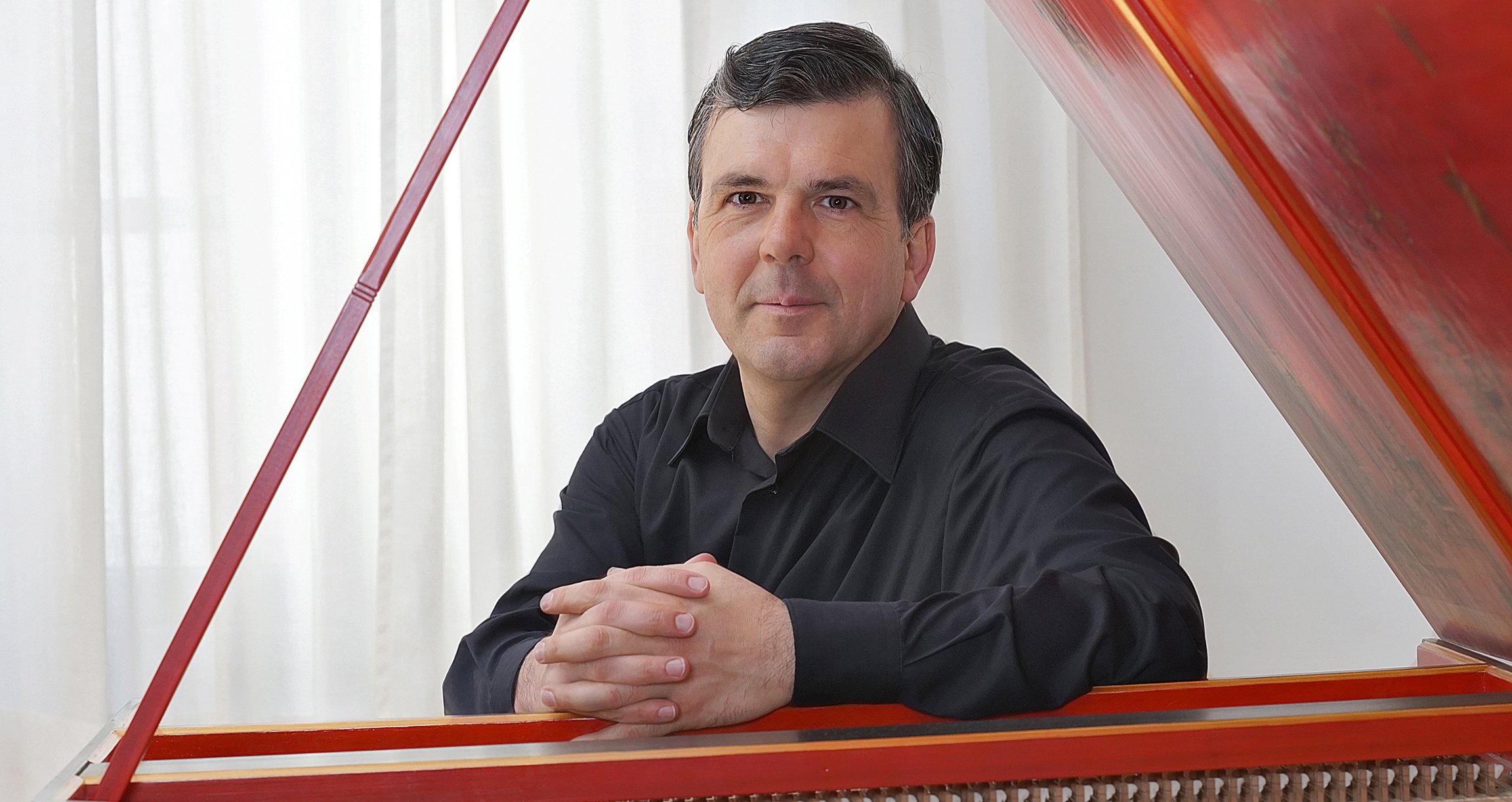 Ein Herr in schwarzem Anzug an Tasteninstrument sitzend