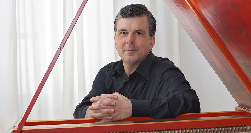 Ein Herr in schwarzem Anzug an Tasteninstrument sitzend