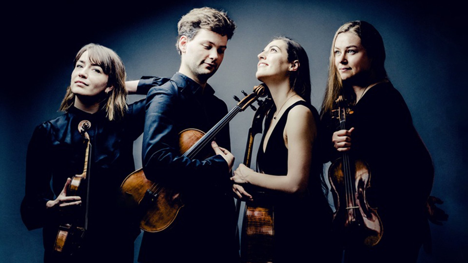 Streichquartett mit vier Musikerinnen und Musikern vor dunklem Studiohintergrund. Die Mitglieder des Barbican Quartet tragen schwarze Konzertkleidung und halten Violinen beziehungsweise ein Cello.