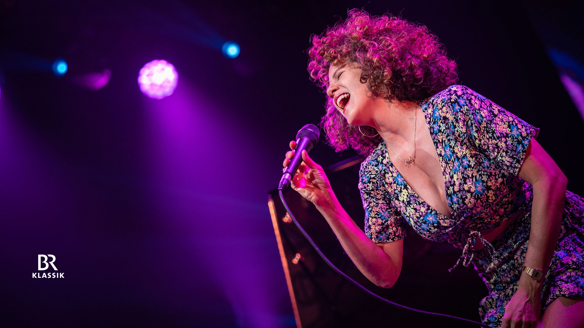 Foto vom Event von Cyrille Aimée mit der Künstlerin mit lockigem Haar, die mit einem Mikrofon singt