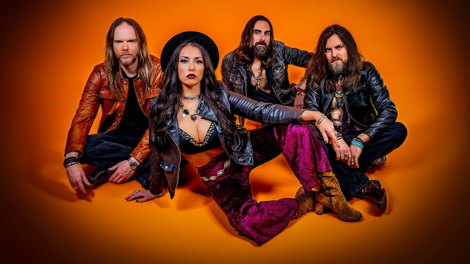 Foto für die Veranstaltung „Velvet Rush“ mit der kompletten Band vor orangem Hintergrund.