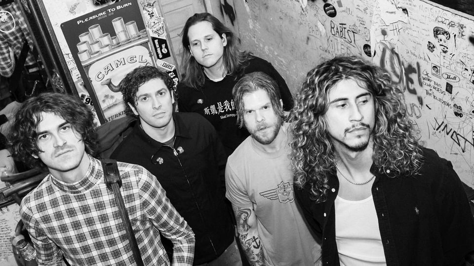 Ein Bild in schwarz-weiss der fünfköpfigen Band Culture Wars in Freizeitkleidung vor einer Wand mit Graffiti