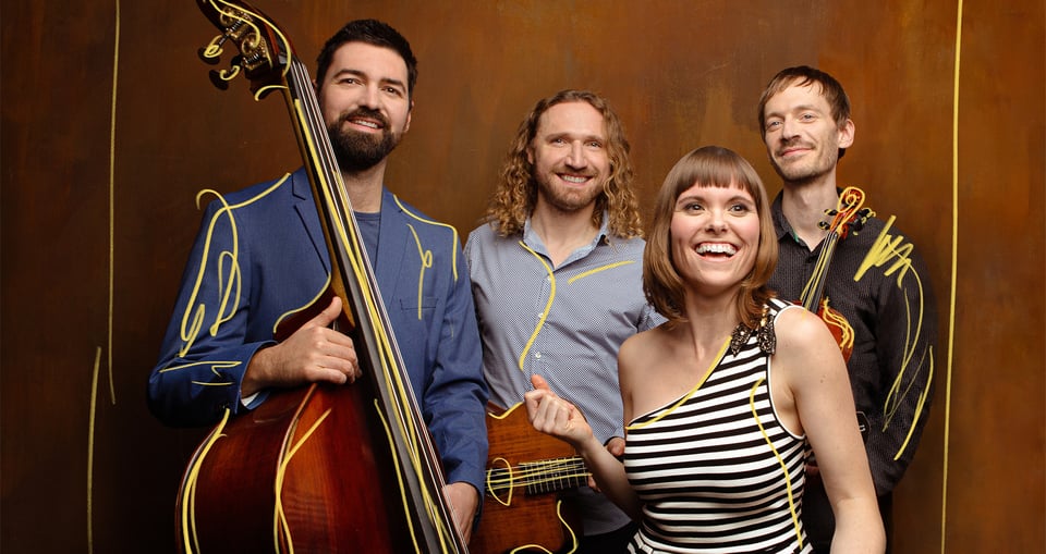 Foto der Gruppe „Marion Sobo Band“ mit drei Jungen und einem Mädchen, mit Instrumenten und einem braunen Hintergrund.