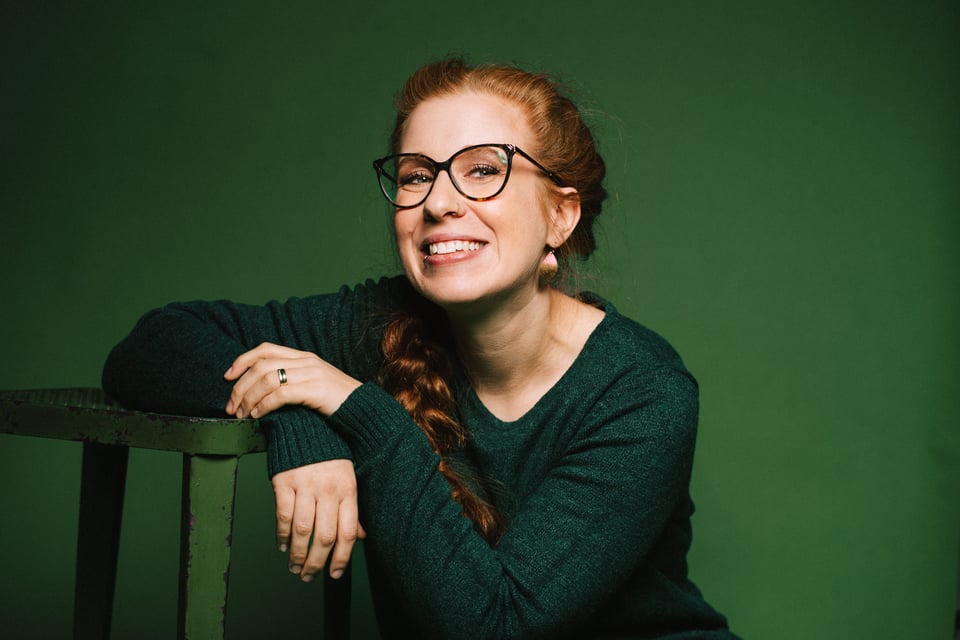 Foto für das Event Sara Brandhuber - A scheena Schmarrn! mit der Künstlerin vor grünem Hintergrund.