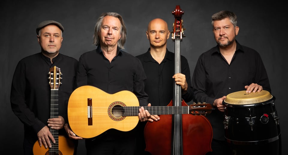 Die Künstler des Corazon Quartett in schwarzer Kleidung mit Instrumenten  stehen vor dunkelgrauem Hintergrund und blicken und die Kamera