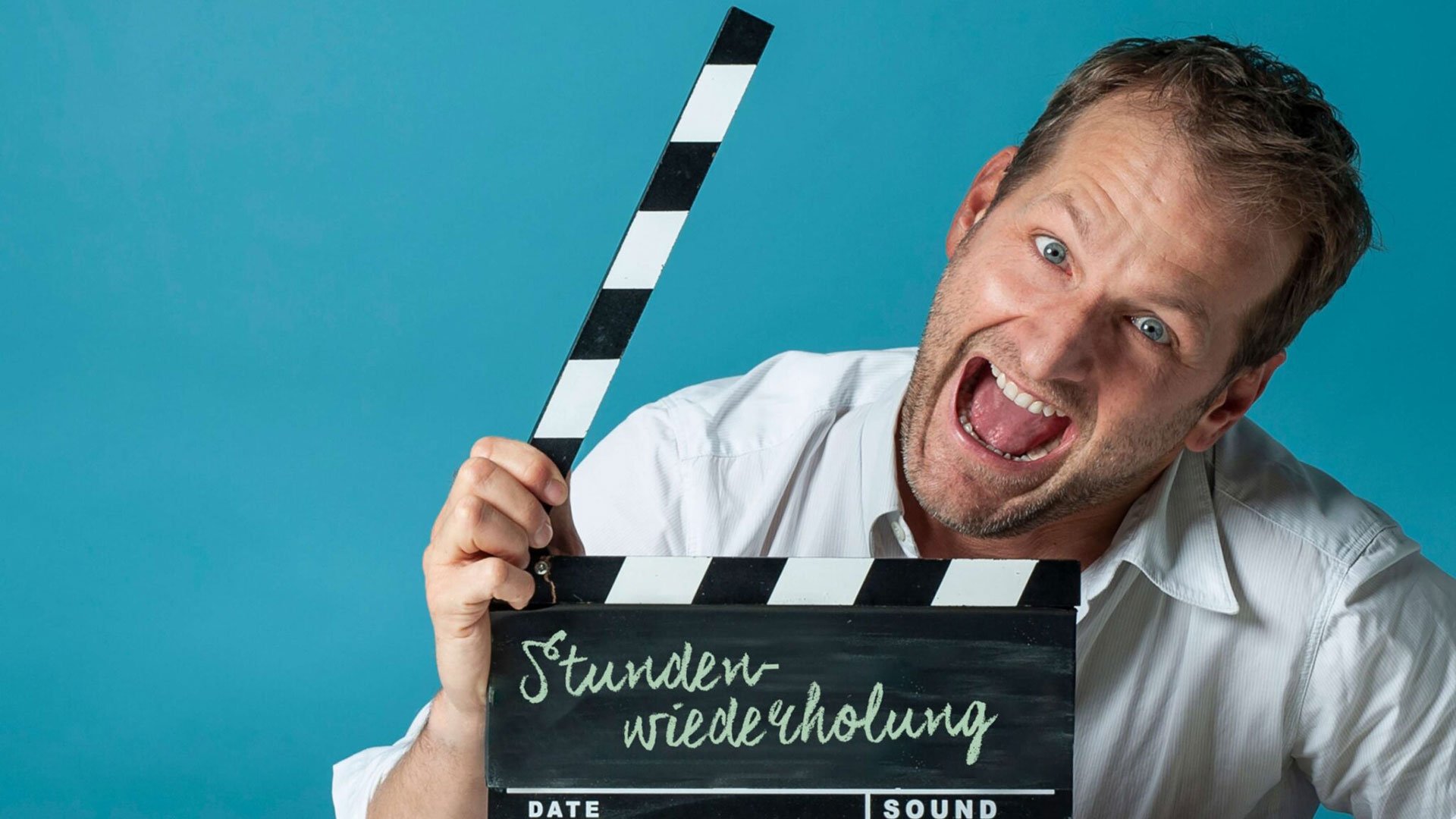 Foto für das Event Andreas Ferner – ‚Stundenwiederholung‘ Best of mit dem Künstler und einer Filmklappe vor blauem Hintergrund.