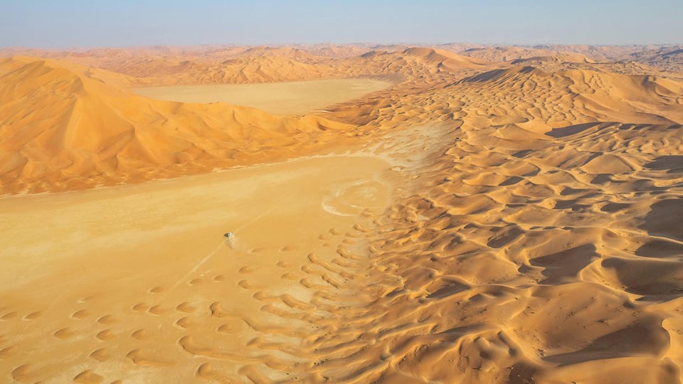 Eine Wüstenlandschaft  mit Sandverwehungen und weit entferntem Horizont und blauem Himmel