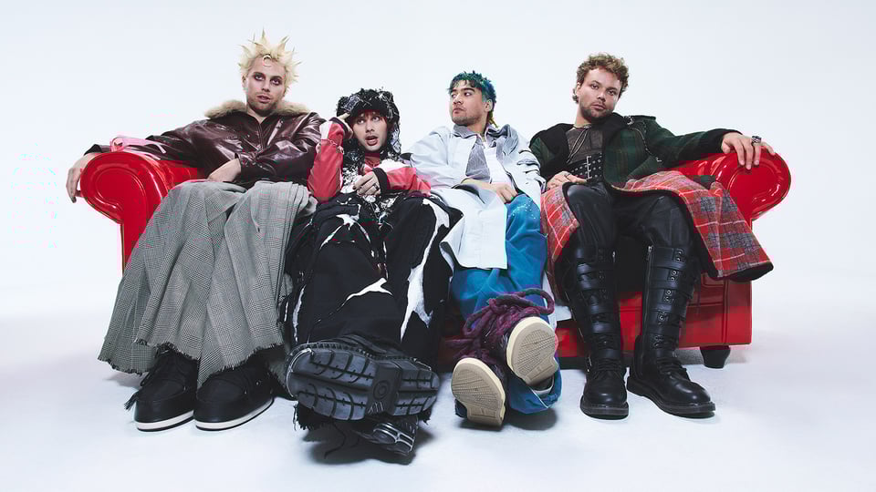 Promofoto für das Event 5 Seconds Of Summer 2026 mit den Künstlern auf einem roten Sofa vor weißem Hintergrund.