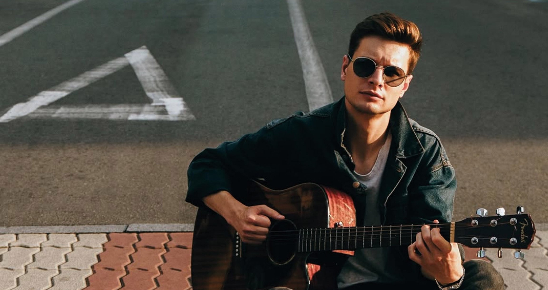 Der Künstler mit Sonnenbrille, am Boden sitzend und Gitarre spielend