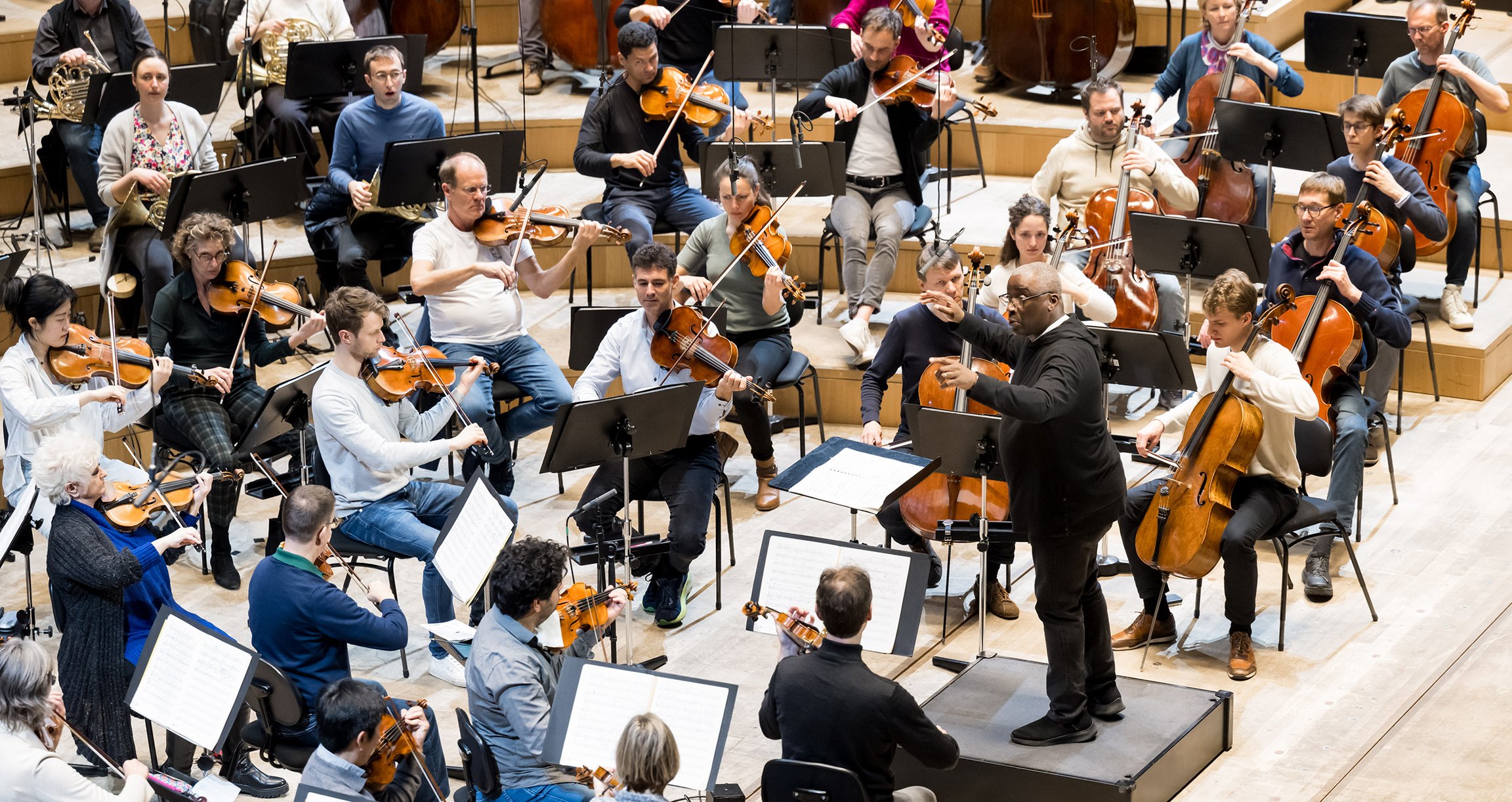 Foto eines Orchesters mit einigen sitzenden Mitgliedern, die ein Instrument spielen 