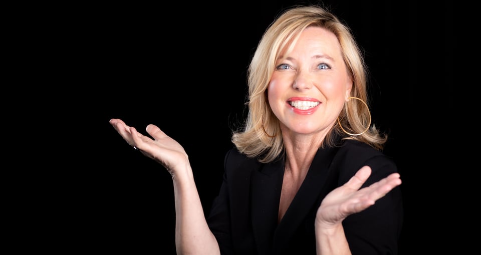 Blonde Dame in schwarzer Kleidung, lachend vor schwarzem Hinterrund