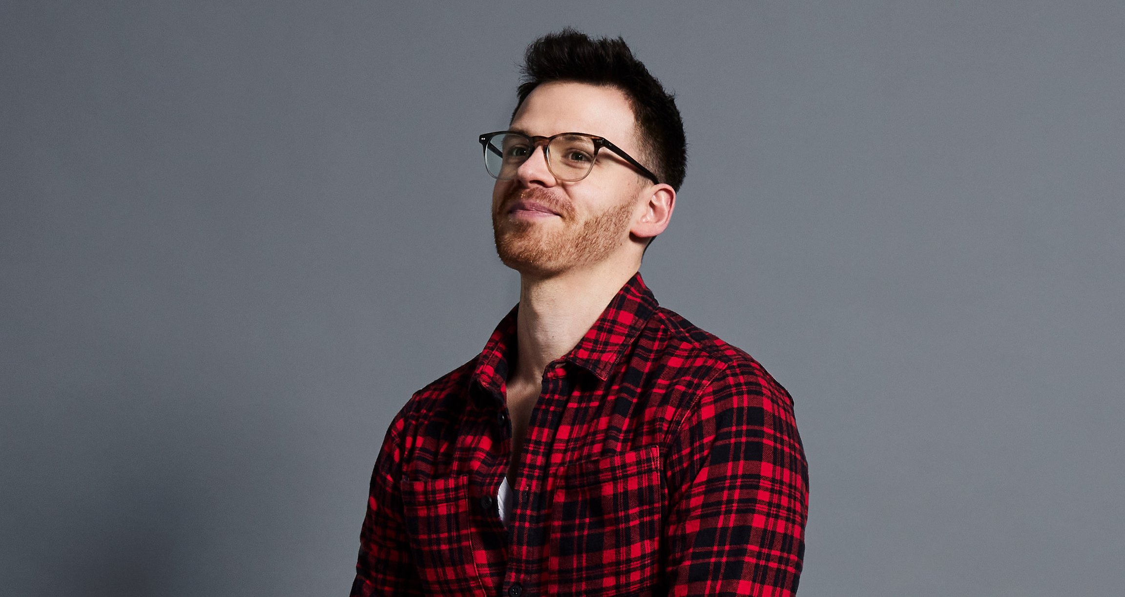 Mann mit Brille und rot-kariertem Hemd vor gauem Hinterrnd