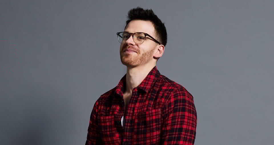 Mann mit Brille und rot-kariertem Hemd vor gauem Hinterrnd