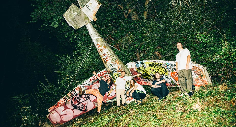 Gruppenfoto mit einem Flugzeug im Hintergrund, das mit Graffiti besprüht ist.