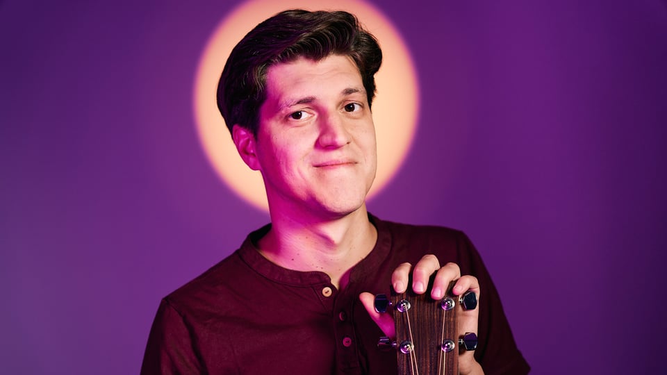 Ein Bild des Künstlers mit Gitarre vor lila Hintergrund